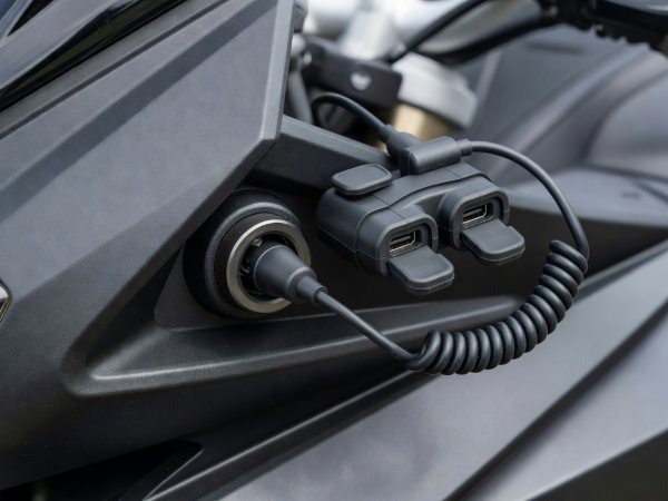 Close-up of DIN ISO 4165 Hella power socket on motorcycle fairing next to dual USB-C weather-capped adapter