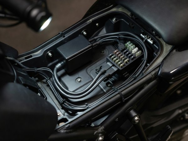 Hardwired motorcycle dual-channel dash camera DVR module installed under seat tray next to fuse block